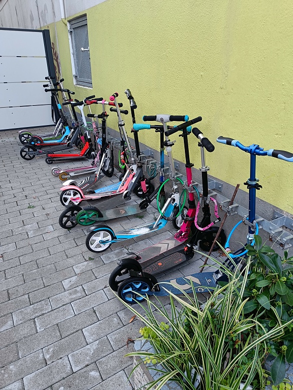 Viele Roller stehen abgestellt am Rollerparkplatz der Schule.