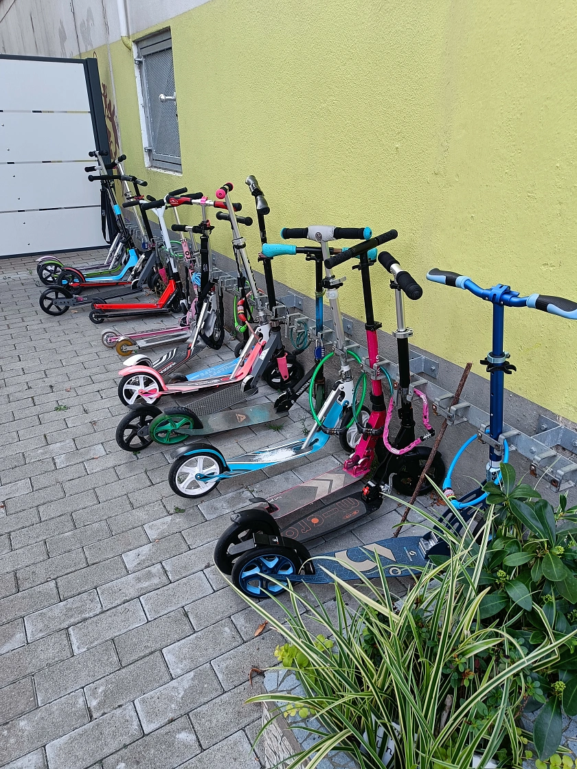 Viele Roller stehen abgestellt am Rollerparkplatz der Schule.