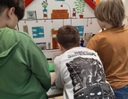 Drei Kinder beugen sich zu einem auf Pappe gemalten Querschnitt eines Hauses.
