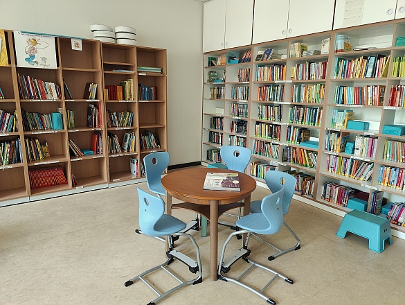 vorne ein runder Tisch mit vier Stühlen drumherum, im Hintergrund viele Bücherregale