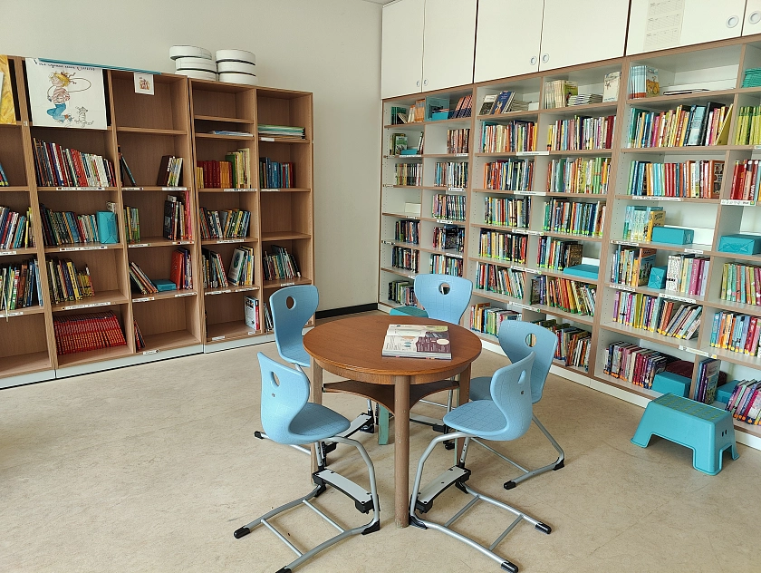 vorne ein runder Tisch mit vier Stühlen drumherum, im Hintergrund viele Bücherregale