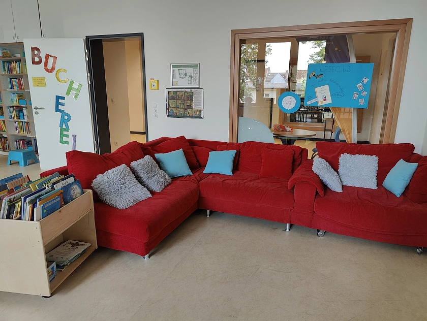 Rotes großes Ecksofa in einer Schulbücherei, Büchertrog links vorne