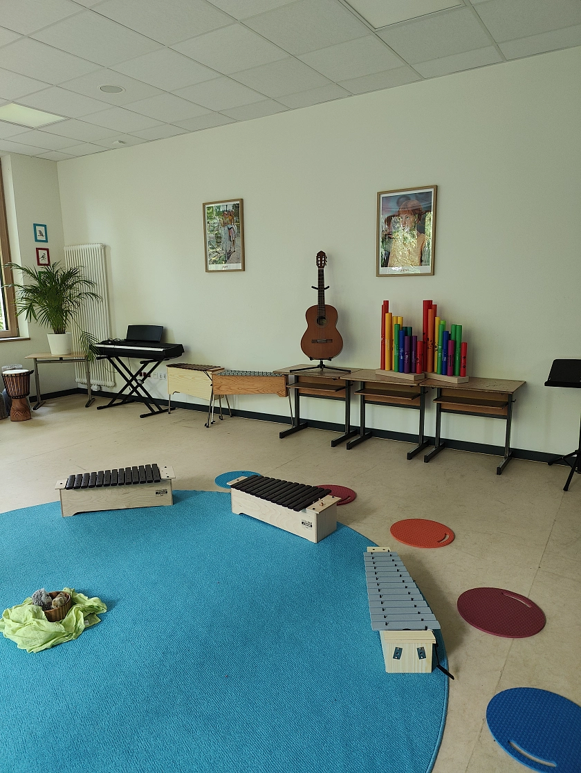 Musikraum mit einem runden Teppich in der Mitte und vielen Instrumenten darum herum