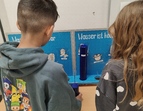 Zwei Kinder stehen mit dem Rücken zum Betrachter. Sie schauen sich eine Stationsarbeit zum Thema Wasserverbrauch an.
